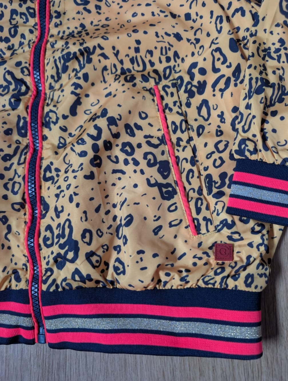 Close-up of the ochre panther jacket showing the neon pink zip and striped hem